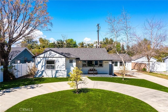 view of front of home with concrete driveway, a front lawn, a shingled roof, and fence