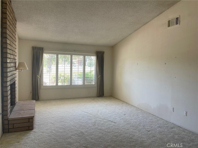 unfurnished room with a textured ceiling, a brick fireplace, carpet flooring, and visible vents