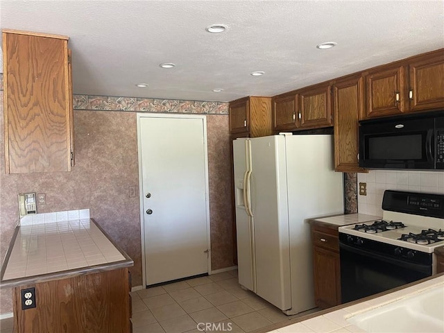 kitchen with black microwave, tile countertops, light tile patterned floors, white refrigerator with ice dispenser, and gas range