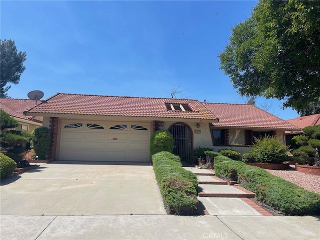 mediterranean / spanish home with concrete driveway, an attached garage, a tiled roof, and stucco siding