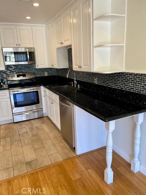 kitchen with light wood finished floors, white cabinets, dark countertops, appliances with stainless steel finishes, and a sink