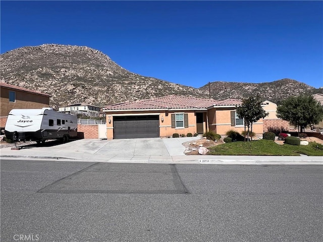 view of front facade with fence, stucco siding, a garage, a tiled roof, and a mountain view