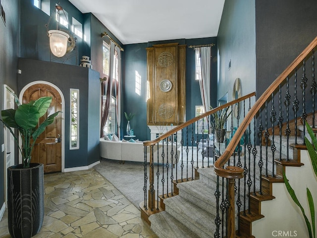 foyer featuring baseboards, stairway, a towering ceiling, and stone tile floors