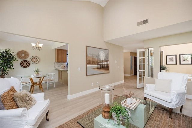 living area with visible vents, baseboards, a high ceiling, light wood-style floors, and a notable chandelier