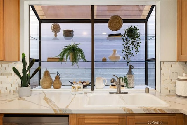 interior space with tasteful backsplash, light stone countertops, dishwasher, brown cabinetry, and a sink