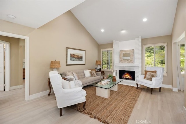 living area with light wood finished floors, a fireplace, high vaulted ceiling, and baseboards