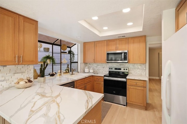 kitchen featuring light stone counters, appliances with stainless steel finishes, light wood-style floors, a raised ceiling, and a sink