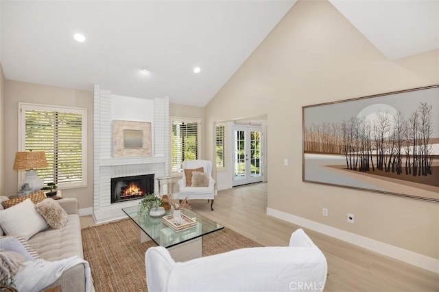 living area with light wood-type flooring, high vaulted ceiling, french doors, baseboards, and a brick fireplace