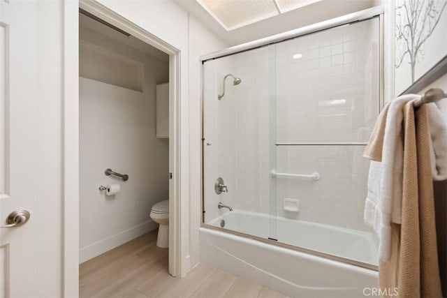 full bath featuring toilet, wood finished floors, combined bath / shower with glass door, and baseboards