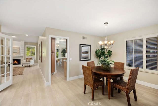 dining room featuring light wood finished floors, visible vents, baseboards, a fireplace, and an inviting chandelier