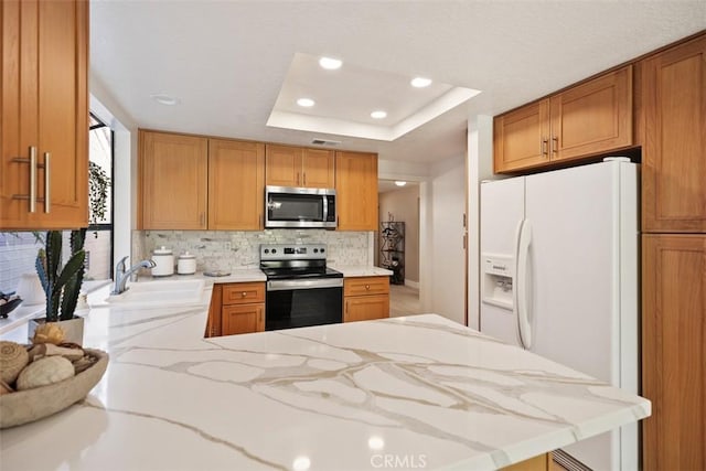 kitchen featuring tasteful backsplash, a tray ceiling, appliances with stainless steel finishes, a peninsula, and a sink