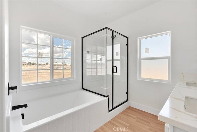 bathroom featuring a stall shower, wood finished floors, a bath, and baseboards