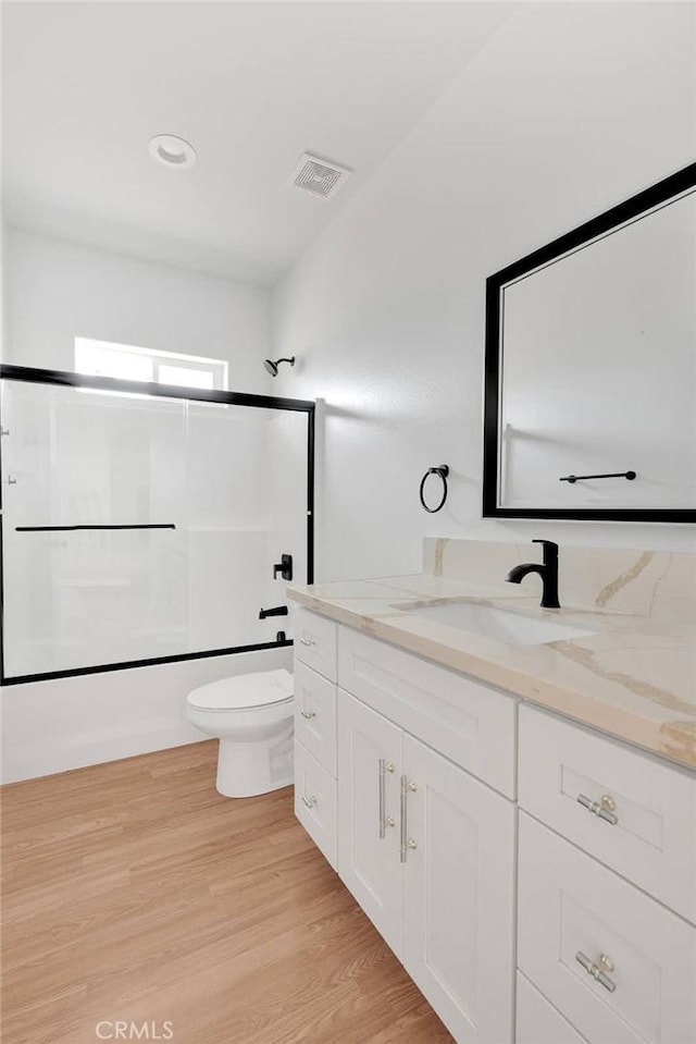 bathroom featuring shower / bath combination, visible vents, toilet, wood finished floors, and vanity