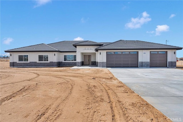 prairie-style home featuring an attached garage, stone siding, a tile roof, and concrete driveway