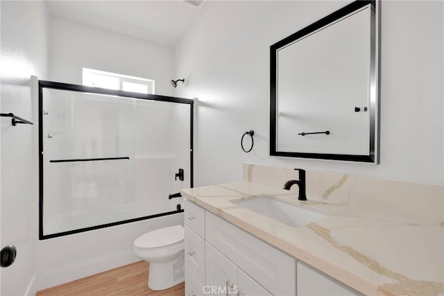 bathroom featuring toilet, bath / shower combo with glass door, wood finished floors, and vanity