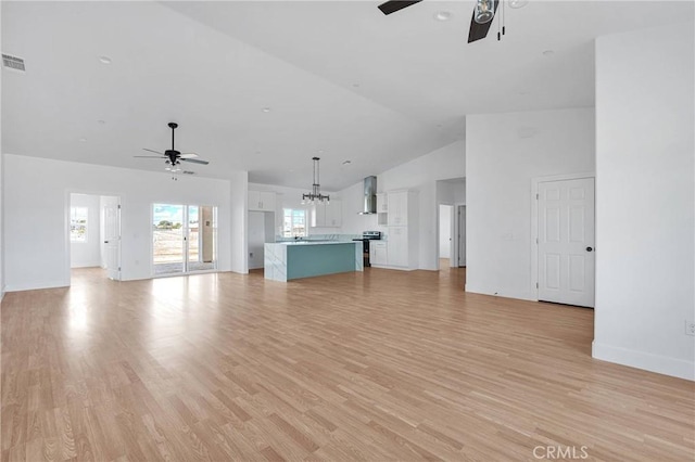 unfurnished living room with high vaulted ceiling, light wood-style flooring, baseboards, and ceiling fan with notable chandelier