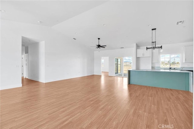 unfurnished living room with ceiling fan with notable chandelier, a wealth of natural light, visible vents, and light wood-style floors