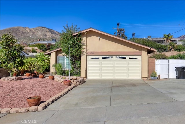 view of front facade featuring fence, a mountain view, concrete driveway, and stucco siding