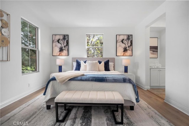 bedroom featuring connected bathroom, baseboards, and wood finished floors