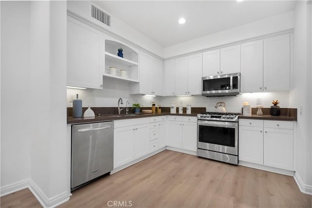 kitchen with visible vents, a sink, stainless steel appliances, light wood-style floors, and dark countertops