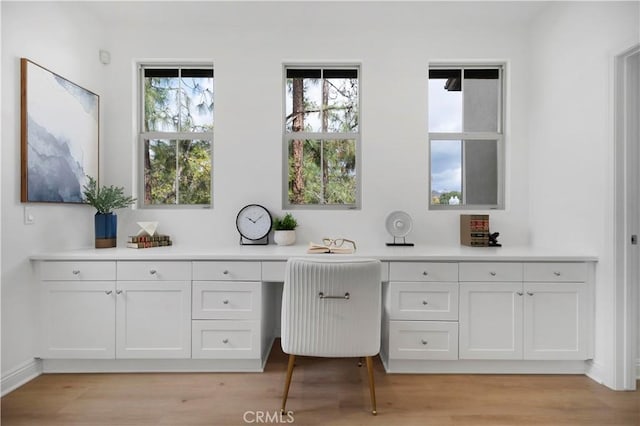 office area with light wood-type flooring, baseboards, and built in desk