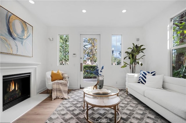 living room featuring recessed lighting, baseboards, a lit fireplace, and wood finished floors