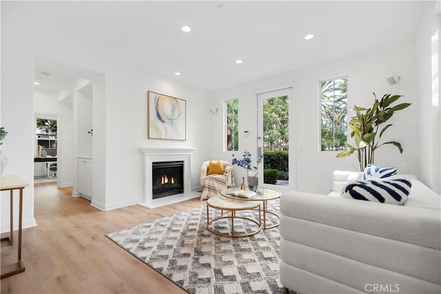 living room featuring recessed lighting, baseboards, light wood-type flooring, and a lit fireplace