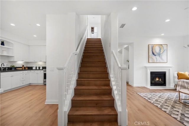 stairway with a glass covered fireplace, wood finished floors, recessed lighting, and visible vents