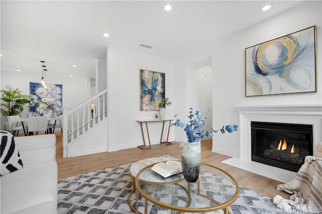 living area with a glass covered fireplace, stairs, visible vents, and wood finished floors