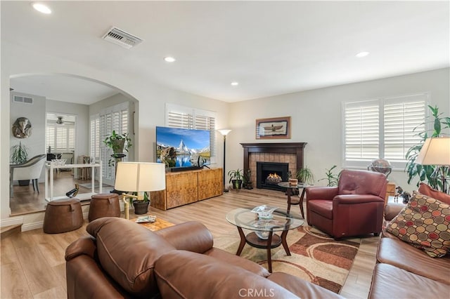 living area featuring a brick fireplace, visible vents, arched walkways, and wood finished floors