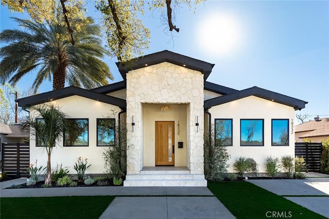 contemporary house featuring stone siding, fence, and stucco siding