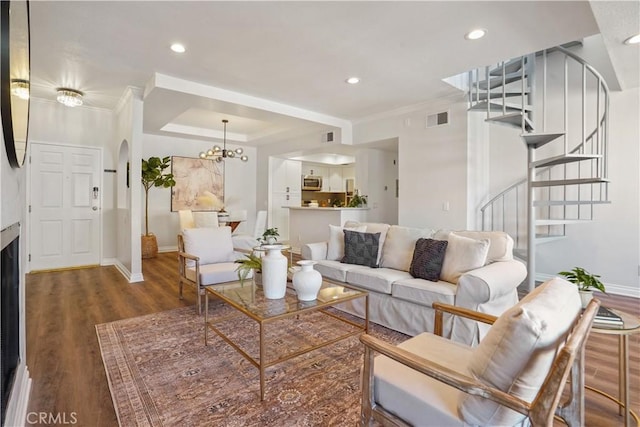 living area with a tray ceiling, dark wood finished floors, visible vents, stairway, and baseboards