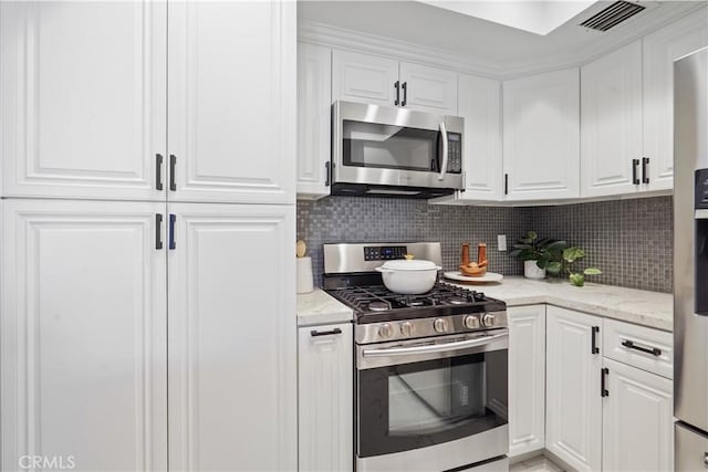 kitchen featuring stainless steel appliances, visible vents, white cabinetry, light stone countertops, and tasteful backsplash