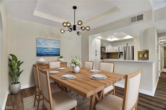 dining space featuring dark wood-style floors, visible vents, a tray ceiling, and baseboards