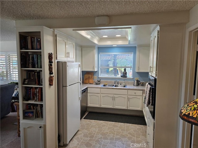 kitchen featuring dishwasher, freestanding refrigerator, a tray ceiling, a sink, and black oven