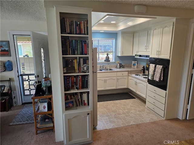 kitchen featuring a textured ceiling, white cabinetry, a sink, and oven