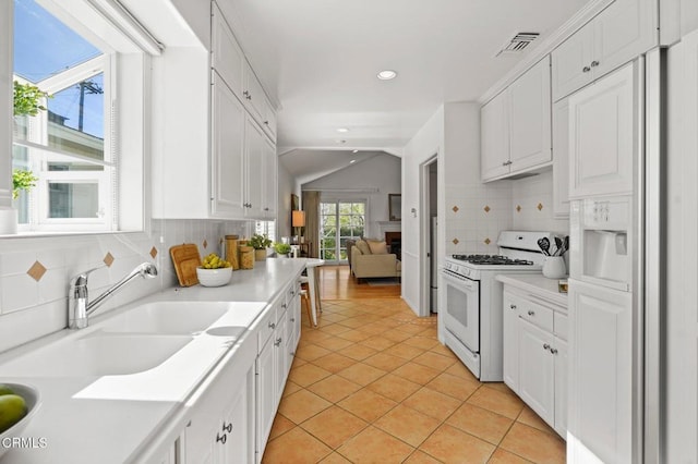 kitchen featuring visible vents, gas range gas stove, lofted ceiling, white cabinets, and a sink