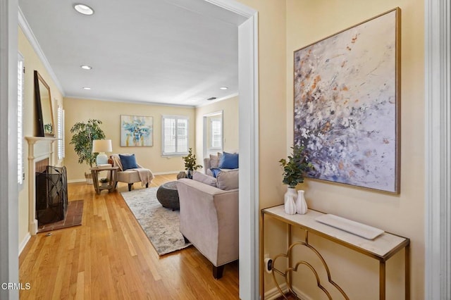 living room featuring light wood finished floors, a fireplace with raised hearth, baseboards, ornamental molding, and recessed lighting