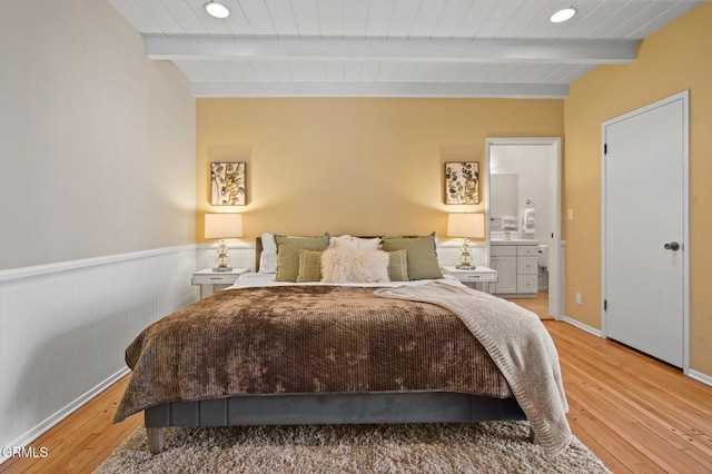 bedroom featuring beam ceiling, connected bathroom, light wood finished floors, and wooden ceiling