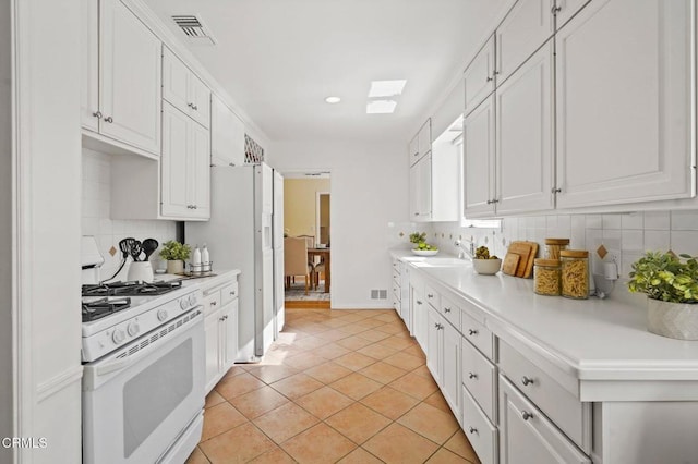 kitchen featuring visible vents, backsplash, white appliances, white cabinets, and light countertops