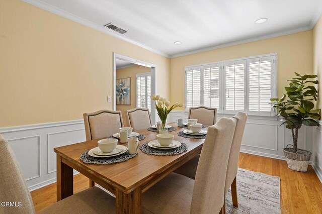 dining room featuring visible vents, wainscoting, light wood-type flooring, and crown molding