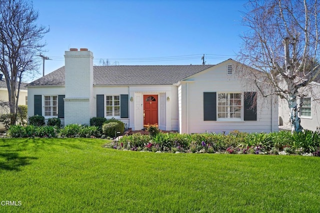 ranch-style home featuring brick siding, a chimney, a front yard, and roof with shingles