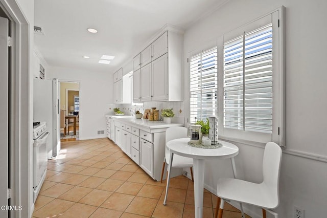 kitchen with visible vents, backsplash, white gas stove, light countertops, and light tile patterned floors