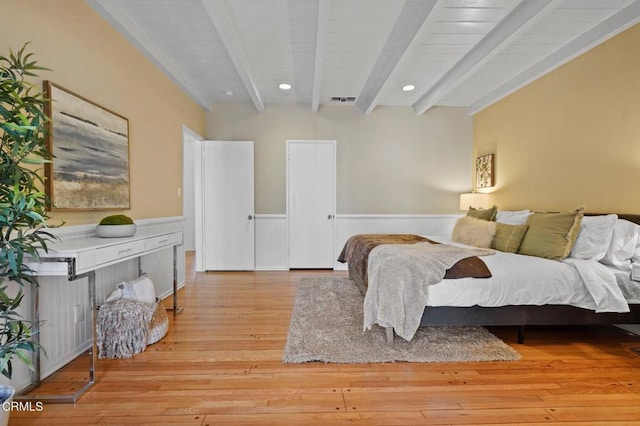 bedroom with light wood-type flooring, a wainscoted wall, beamed ceiling, visible vents, and recessed lighting