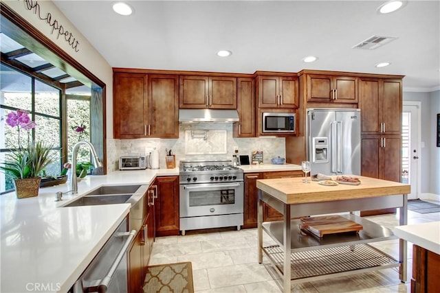 kitchen with under cabinet range hood, a sink, visible vents, high quality appliances, and decorative backsplash