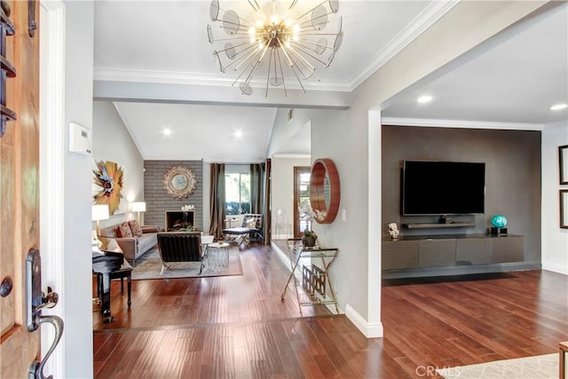 foyer entrance featuring a brick fireplace, ornamental molding, a chandelier, and wood finished floors