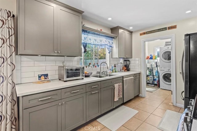 kitchen featuring a sink, stainless steel dishwasher, gray cabinets, freestanding refrigerator, and stacked washer and clothes dryer