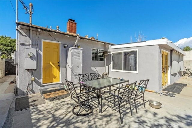 rear view of property with entry steps, a patio area, a chimney, and stucco siding