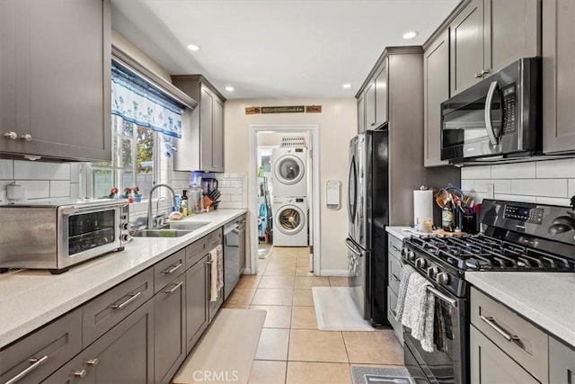 kitchen featuring light tile patterned floors, a toaster, stacked washer and dryer, a sink, and appliances with stainless steel finishes