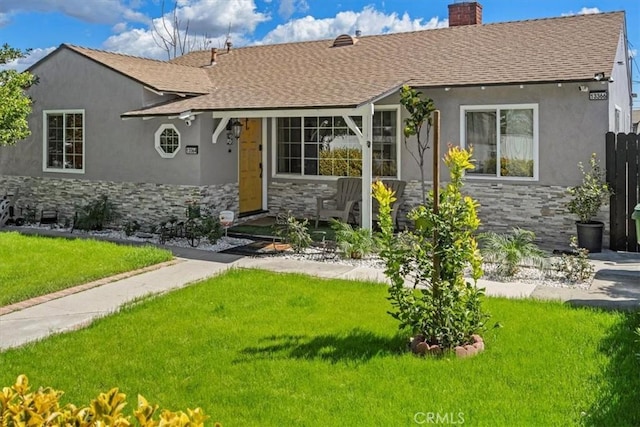 view of front of home featuring stone siding, roof with shingles, a chimney, and a front lawn